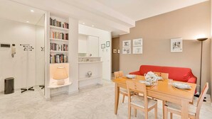 Un salon moderne avec un coin repas, comprenant un canapé rouge, une table à manger en bois et une bibliothèque remplie de livres.