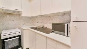 Une cuisine de taille réduite avec des meubles blancs, un four à micro-ondes encastré, une cuisinière et un évier.
