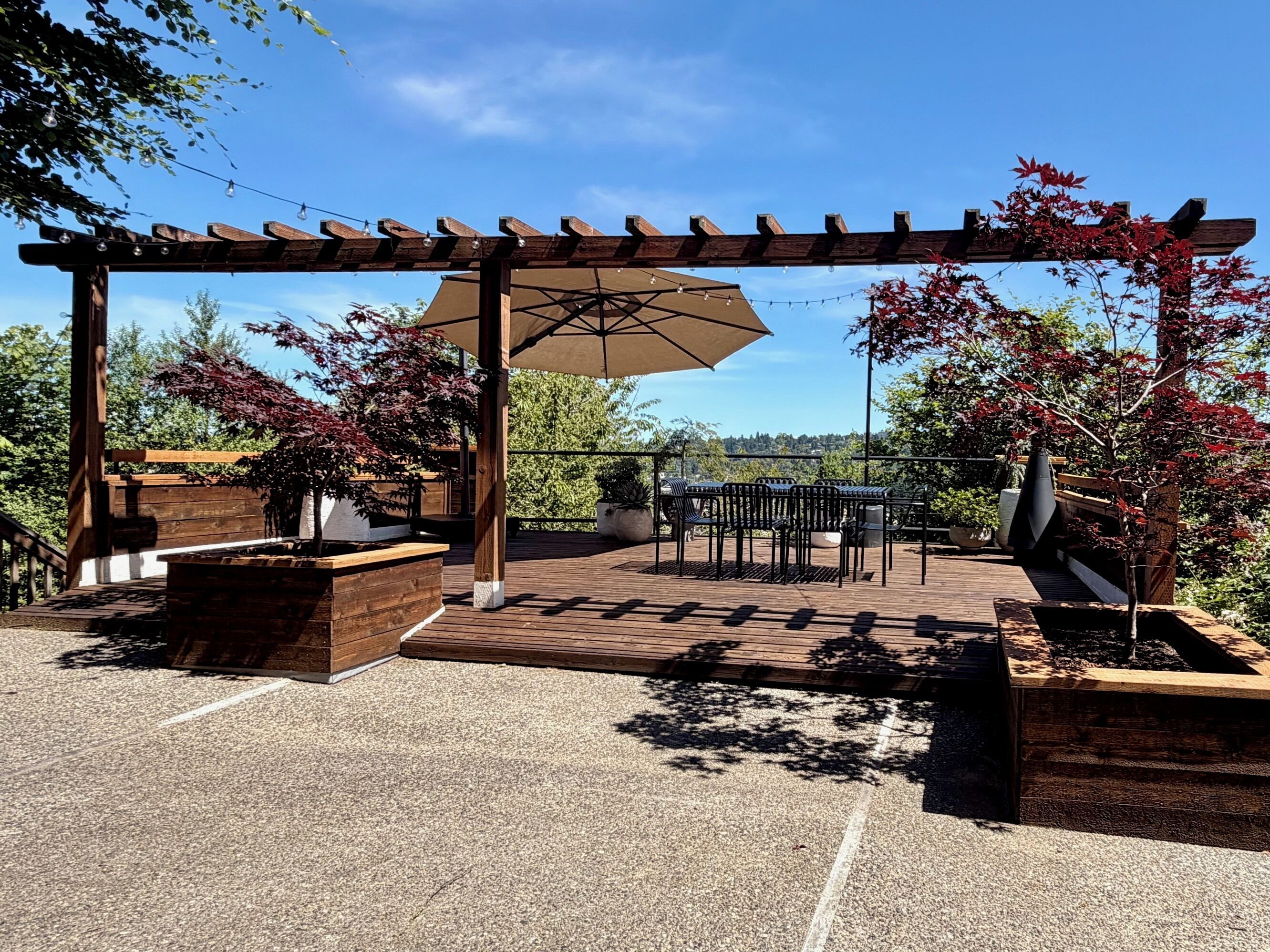 En udendørs terrasse med pergola, siddepladser og plantekasser.
