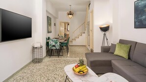 En moderne stue med et fladskærms TV, en grå sofa, et spisebord med stole og en trappe til et andet niveau.