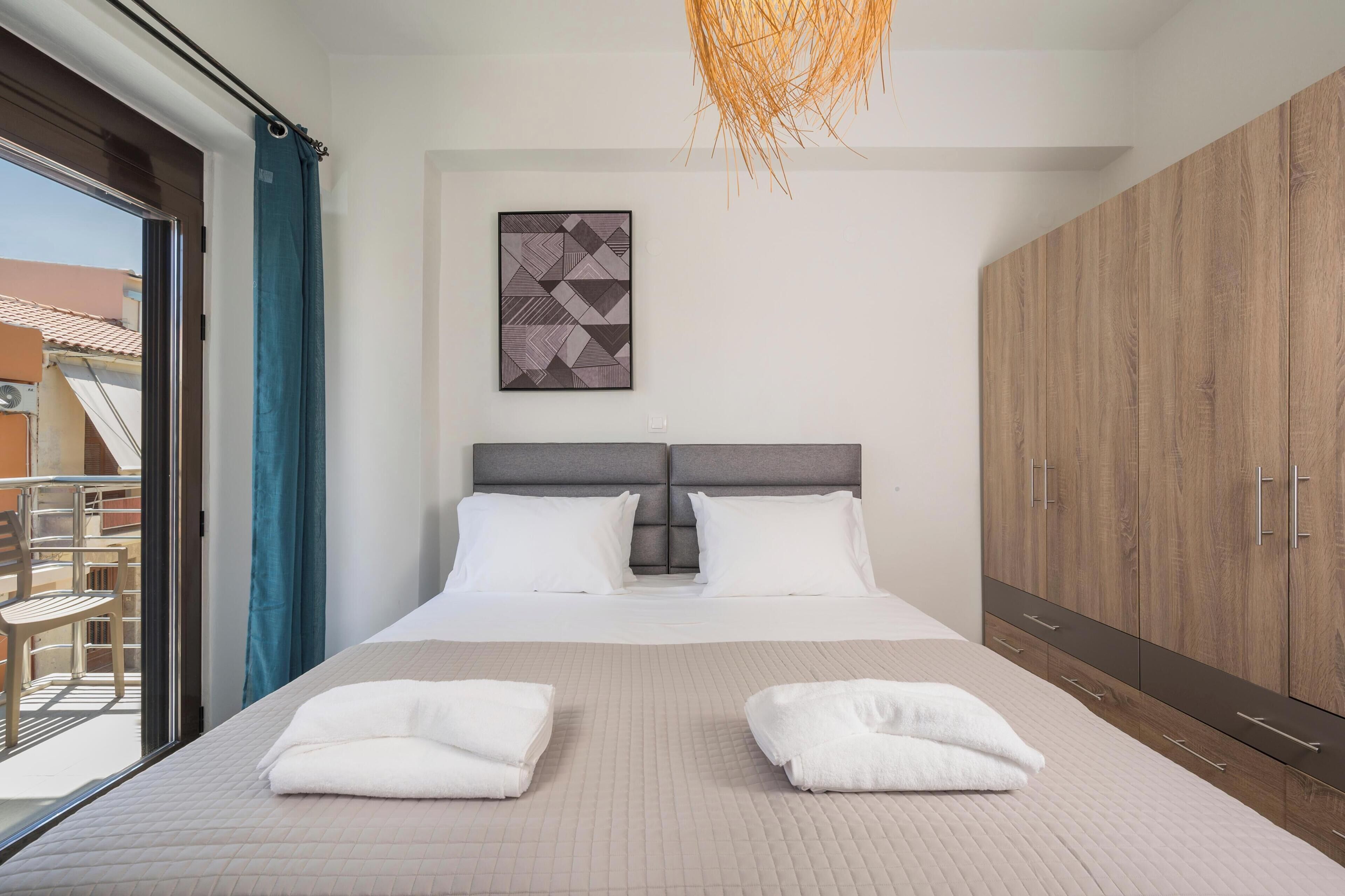 Une chambre d’hôtel avec un grand lit, une armoire en bois, un luminaire au plafond et une vue sur le balcon extérieur.