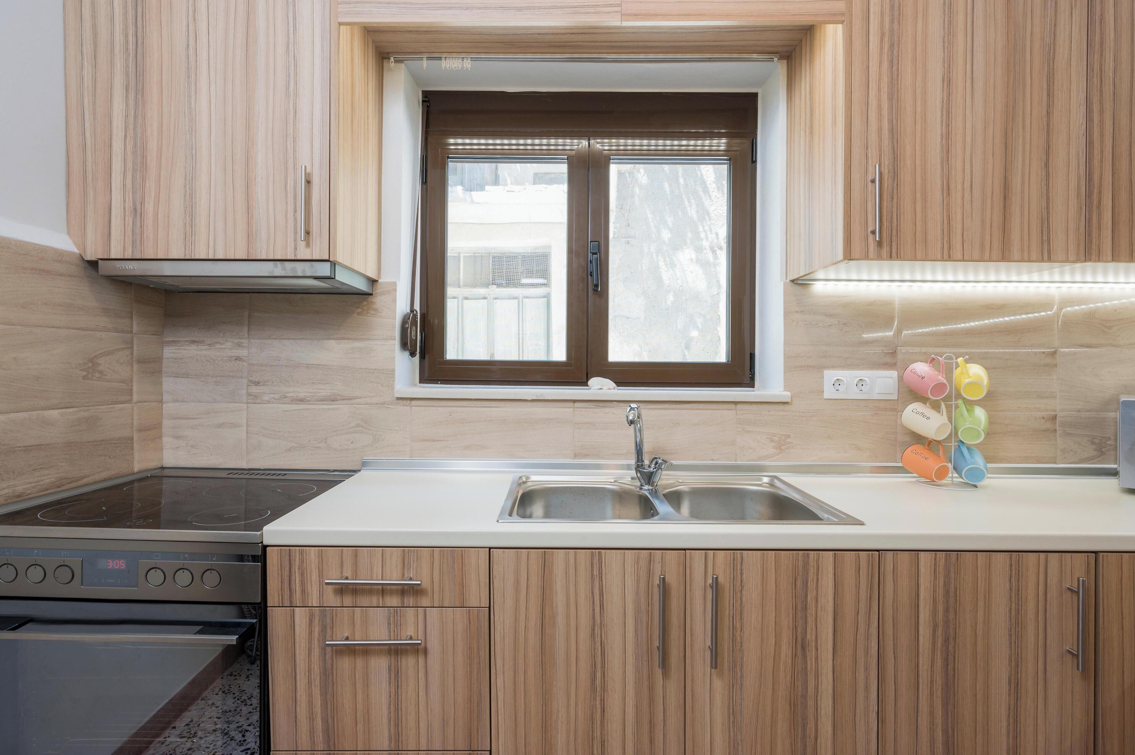 Una cocina moderna con armarios de madera, un lavamanos de acero inoxidable y una ventana sobre la encimera.