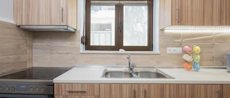 Una cocina moderna con armarios de madera, un lavamanos de acero inoxidable y una ventana sobre la encimera.