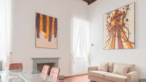A spacious living room with a glass table, a beige sofa, and a fireplace. - Nosdom Properties - Piazza Navona Design Apartment (Roma)