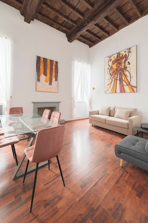 A spacious living room with a glass table, a beige sofa, and a fireplace. - Nosdom Properties - Piazza Navona Design Apartment (Roma)