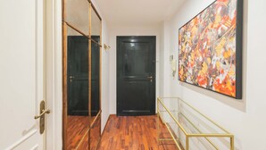 A hallway with a wooden floor, a black door, and a large abstract painting on the wall. - Nosdom Properties - Piazza Navona Design Apartment (Roma)