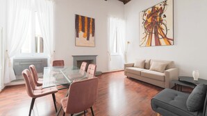 A spacious living room with a glass dining table, a sofa, and a fireplace. - Nosdom Properties - Piazza Navona Design Apartment (Roma)