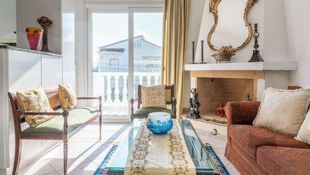 Un salon comprenant un canapé, un fauteuil, une table basse en verre avec un récipient, une cheminée et un balcon avec une balustrade.