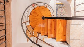 Un escalier en colimaçon avec des marches en bois et des rampes en métal, menant à l’étage supérieur.