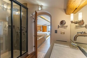 A modern bathroom with a glass shower enclosure, a wooden-framed door, and a large mirror with wall-mounted lights. - Historical Palace with pool (Città della Pieve)