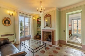 A living room with a glass coffee table, a fireplace, a bookshelf, and a large window. - Historical Palace with pool (Città della Pieve)