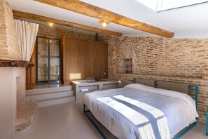 Ein Schlafzimmer mit einem großen Bett, Holzboden, Steinwand und einem Vorhangfenster.
