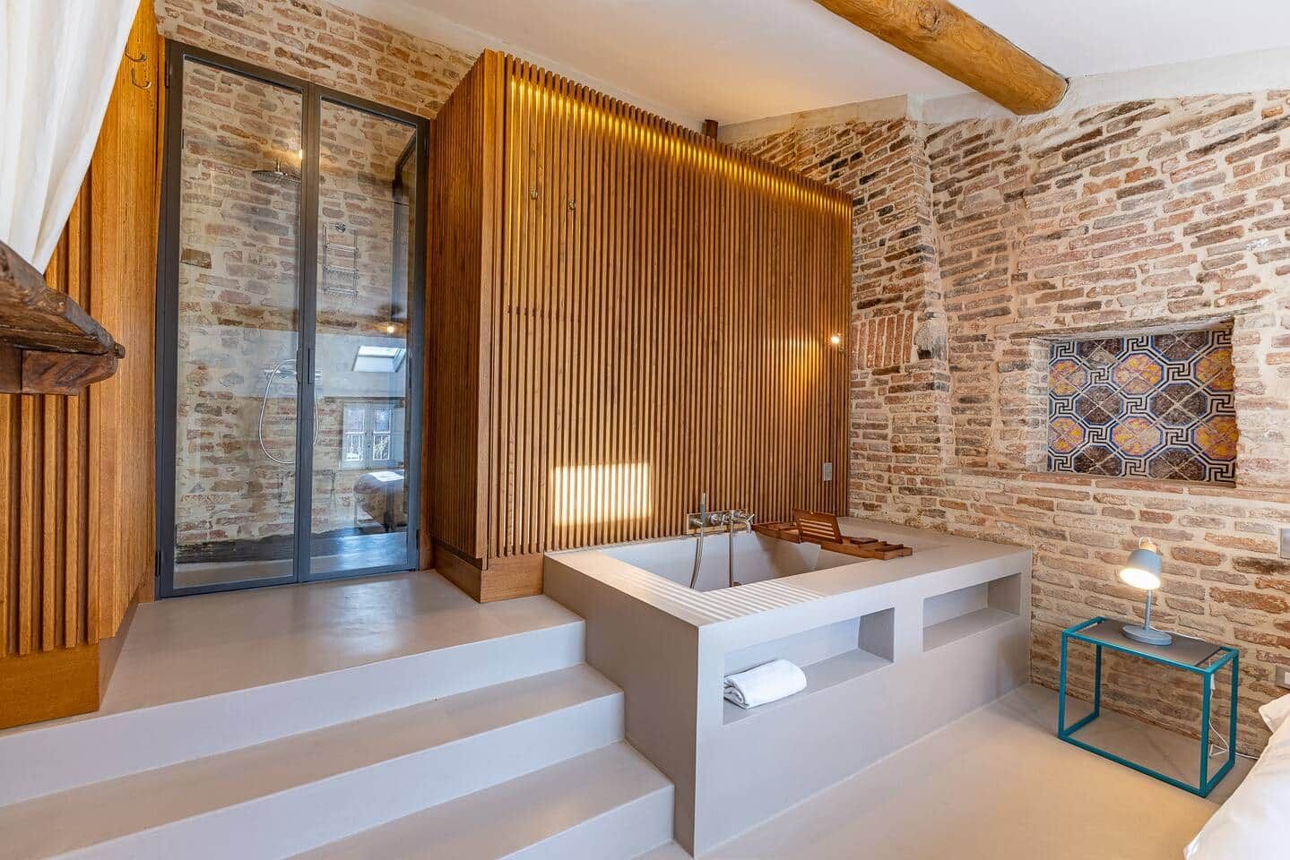 A modern bathroom with a stone wall, a wooden slatted partition, and a large bathtub.
