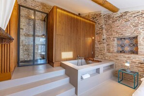 Ein modernes Badezimmer mit Steinwand, Holzlattenverkleidung und einer großen Badewanne.