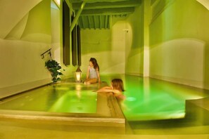 Un spa con una piscina iluminada en verde, un farol y una planta.