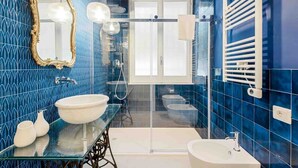 Un baño con azulejos azules, dos lavamanos, una ducha con cerramiento de vidrio y un espejo con un marco decorado.