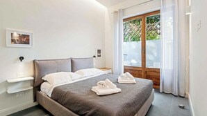 Un dormitorio moderno con una cama grande, una mesita de noche, una ventana con cortinas y vistas a zonas verdes.