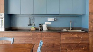Una cocina compacta con armarios azules, una cafetera, un hervidor y un fregadero.