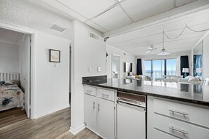 A modern kitchen with white cabinetry, a granite countertop, and a view of the living area. - Two bedroom, two bath oceanfront escape on 126th Street (Ocean City)