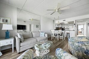 A living room with a sofa, coffee table, and patterned armchair. A dining area with a table and chairs is visible in the background. - Two bedroom, two bath oceanfront escape on 126th Street (Ocean City)
