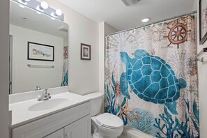 Een badkamer met een wit wastafel, spiegel en toilet. Er is een douchegordijn met een zeeschildpad dessin.