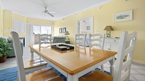 Un comedor con mesa de madera, sillas blancas y un ventilador de techo.