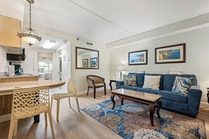 Een woonkamer met een blauwe bank, een houten bijzettafeltje en een kamerkleed met dessin.