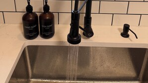 Uma pia de cozinha com uma torneira moderna, duas embalagens de sabonete líquido para as mãos e uma embalagem de detergente.