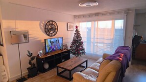 Ein Wohnzimmer mit einer Couch, einem Couchtisch, einem Fernseher, einem Weihnachtsbaum und einem Fenster mit Vorhängen.