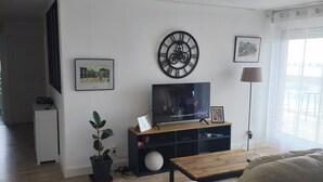 Ein Wohnzimmer mit Fernseher, einer Uhr, einer Pflanze und einem Sofa.