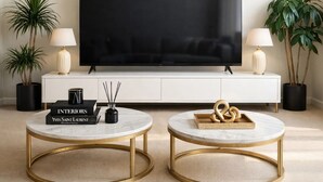 A modern living room with a large flat-screen TV, two round marble coffee tables with gold frames, a white cabinet, and two potted plants. - Luxury Sanctuary in Covent Garden | 3 Beds, AC, Wi-Fi (London)