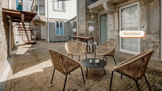 Ein Innenhof mit Korbstühlen und einem Tisch, einer Treppe und einem Gebäude mit einem Balkon.