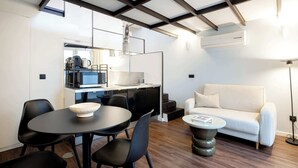 Ein modernes Wohnzimmer mit Sofa, Esstisch, Stühlen und einer Küchenzeile mit Kaffeemaschine.