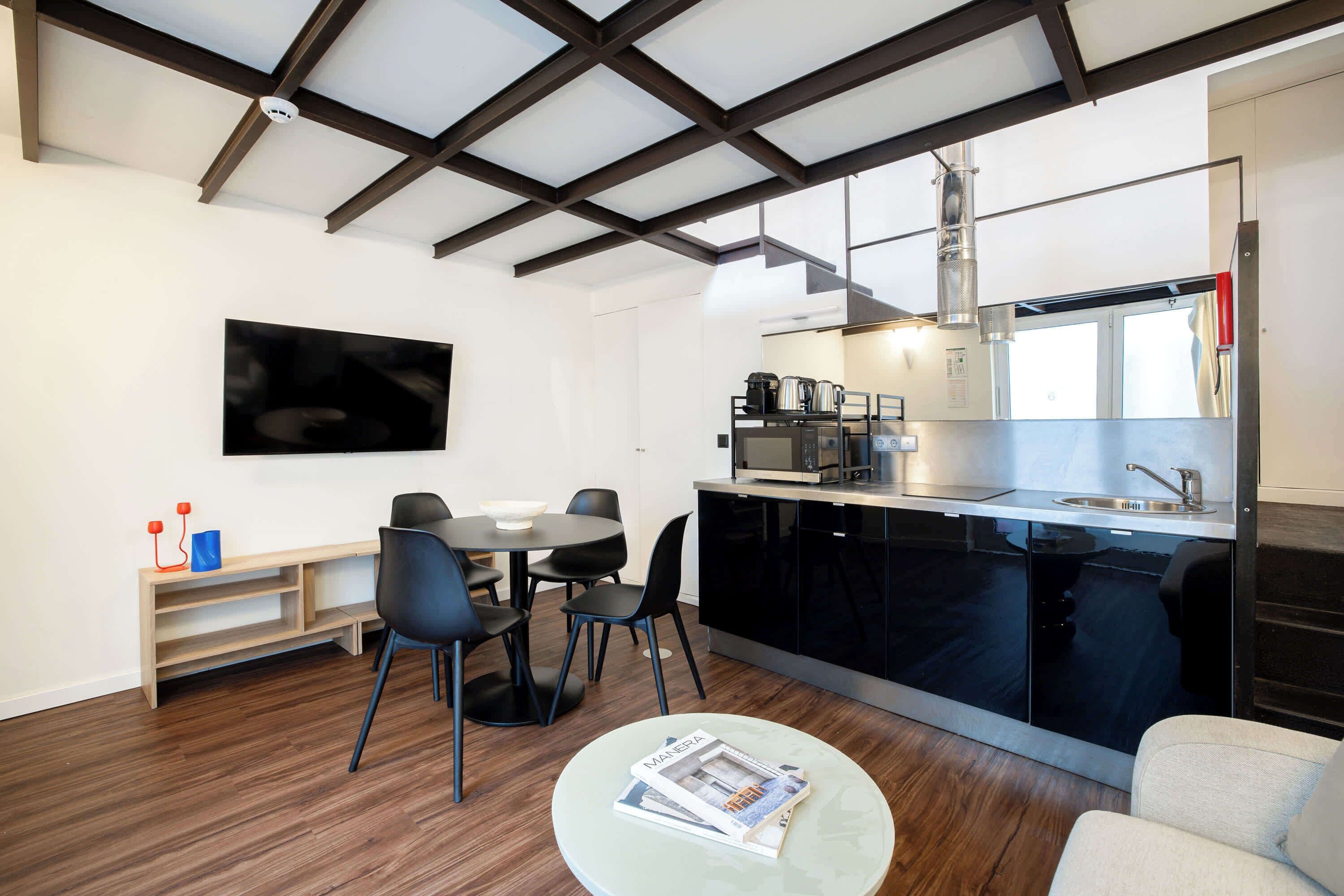 A modern kitchen with a built-in stove, a dining area with a table and chairs, and a flat-screen TV mounted on the wall.