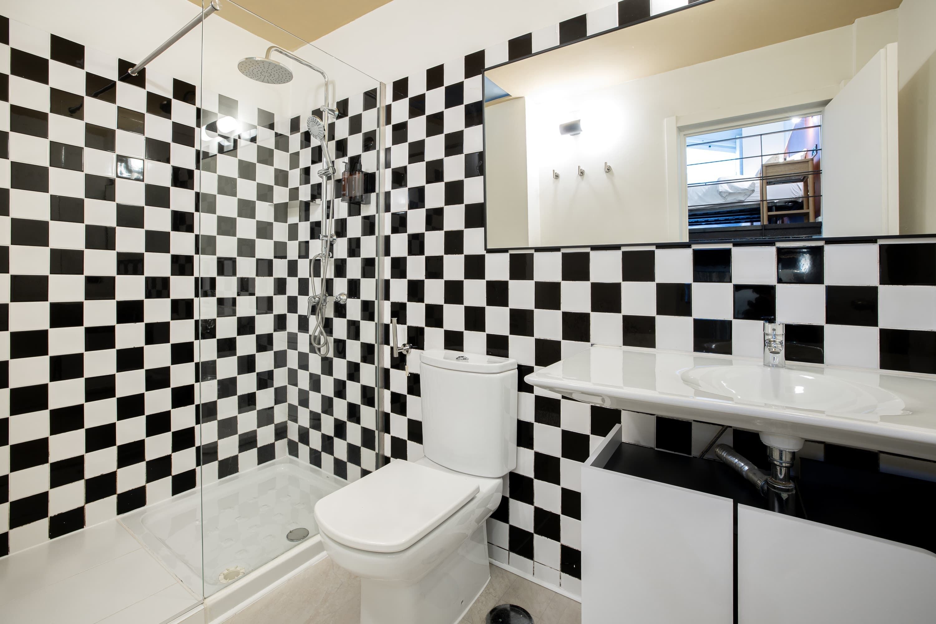A modern bathroom with a checkered black and white tile wall, a white toilet, a glass-enclosed shower, and a white sink with a mirror above it.