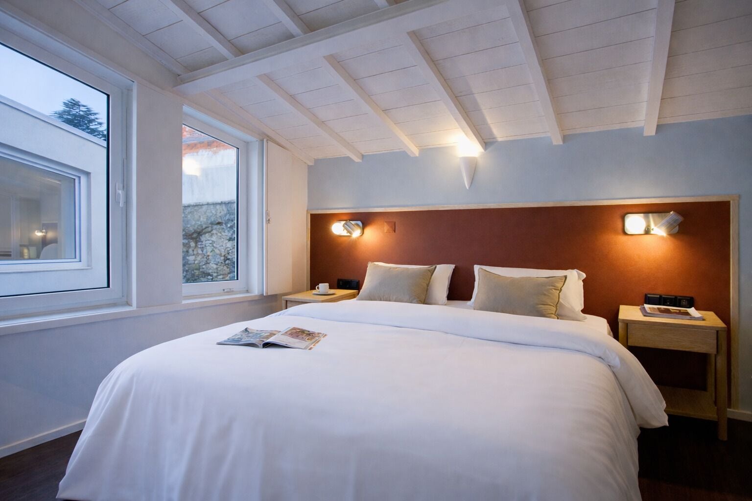 A hotel room with a large bed, two bedside tables, a window, and a wooden ceiling.