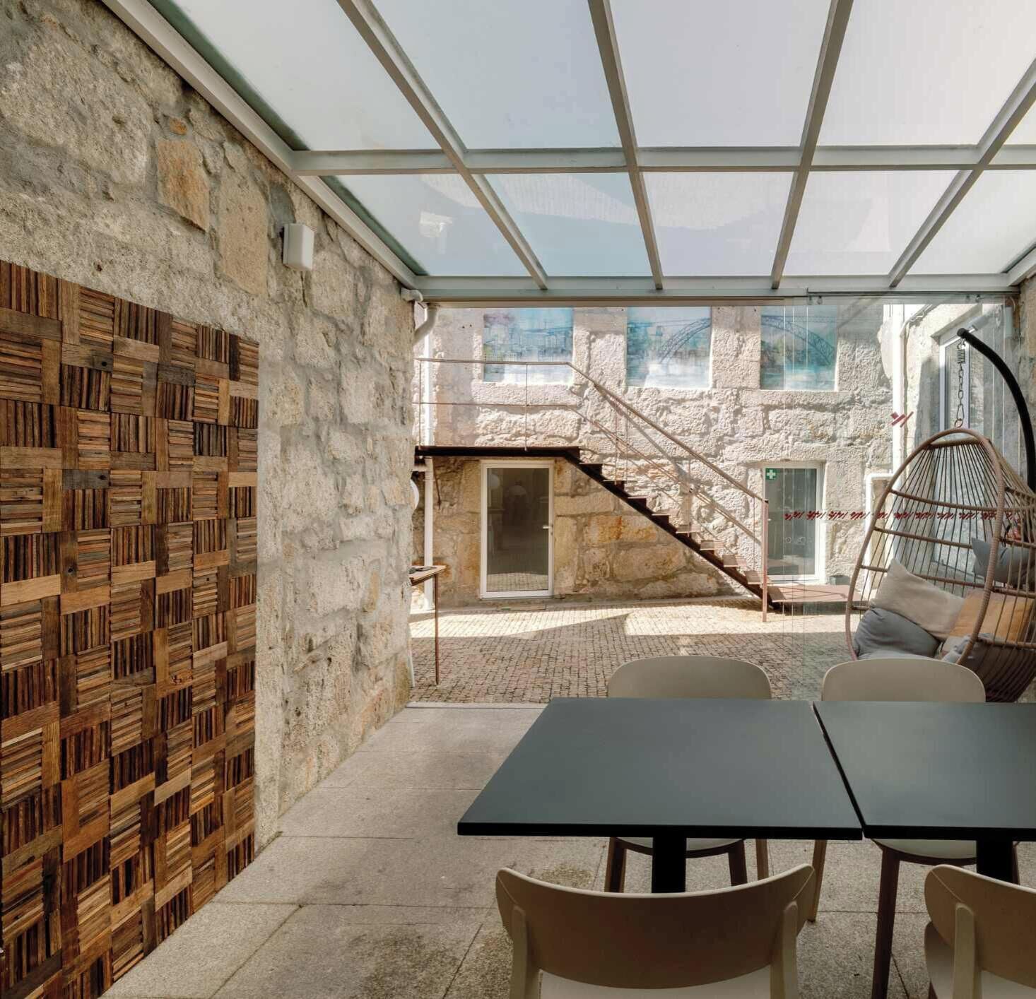A modern outdoor patio with a stone wall, a glass ceiling, and a staircase leading to an upper level.