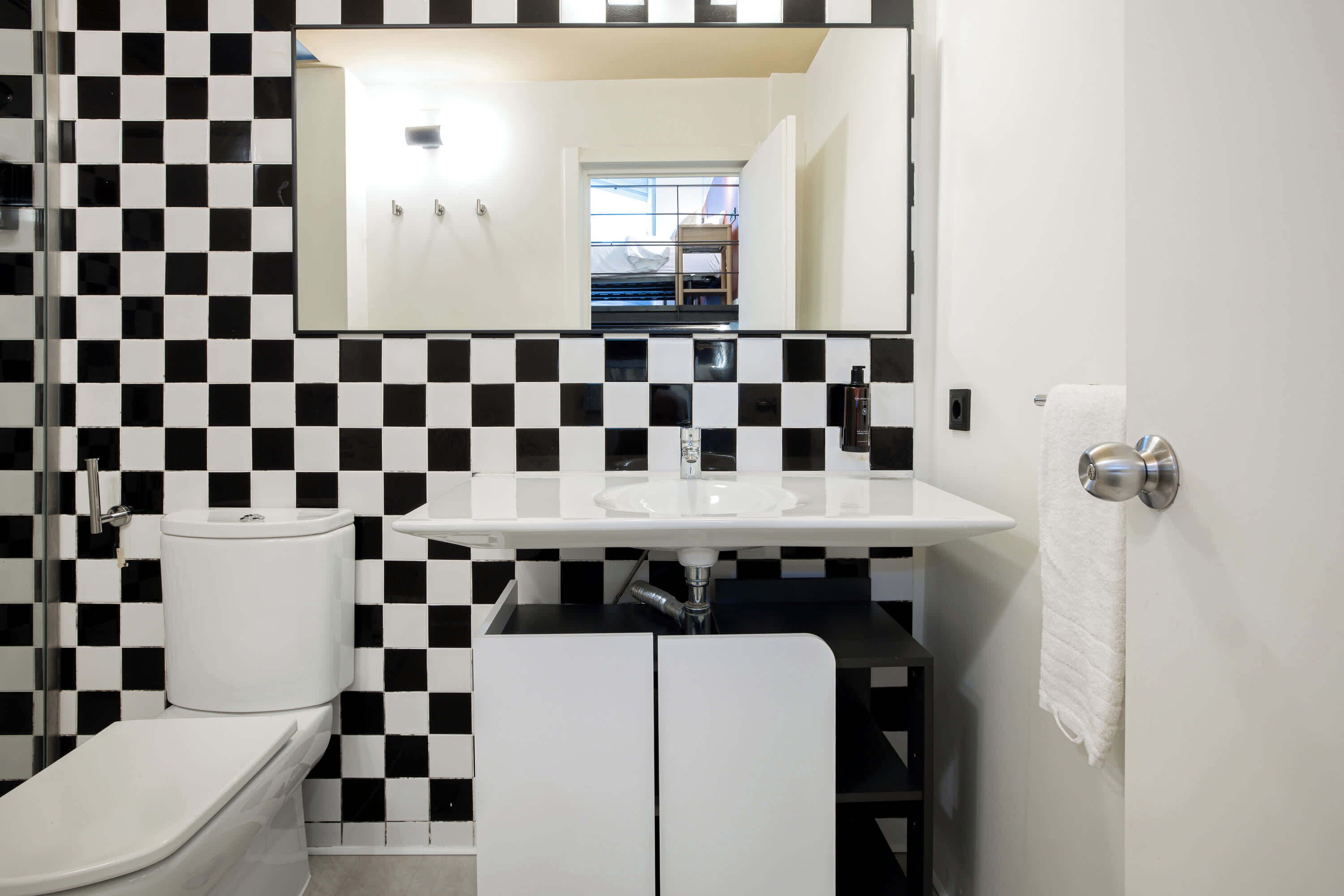 A bathroom with a black and white checkered wall pattern, a white sink, a toilet, and a mirror above the sink.