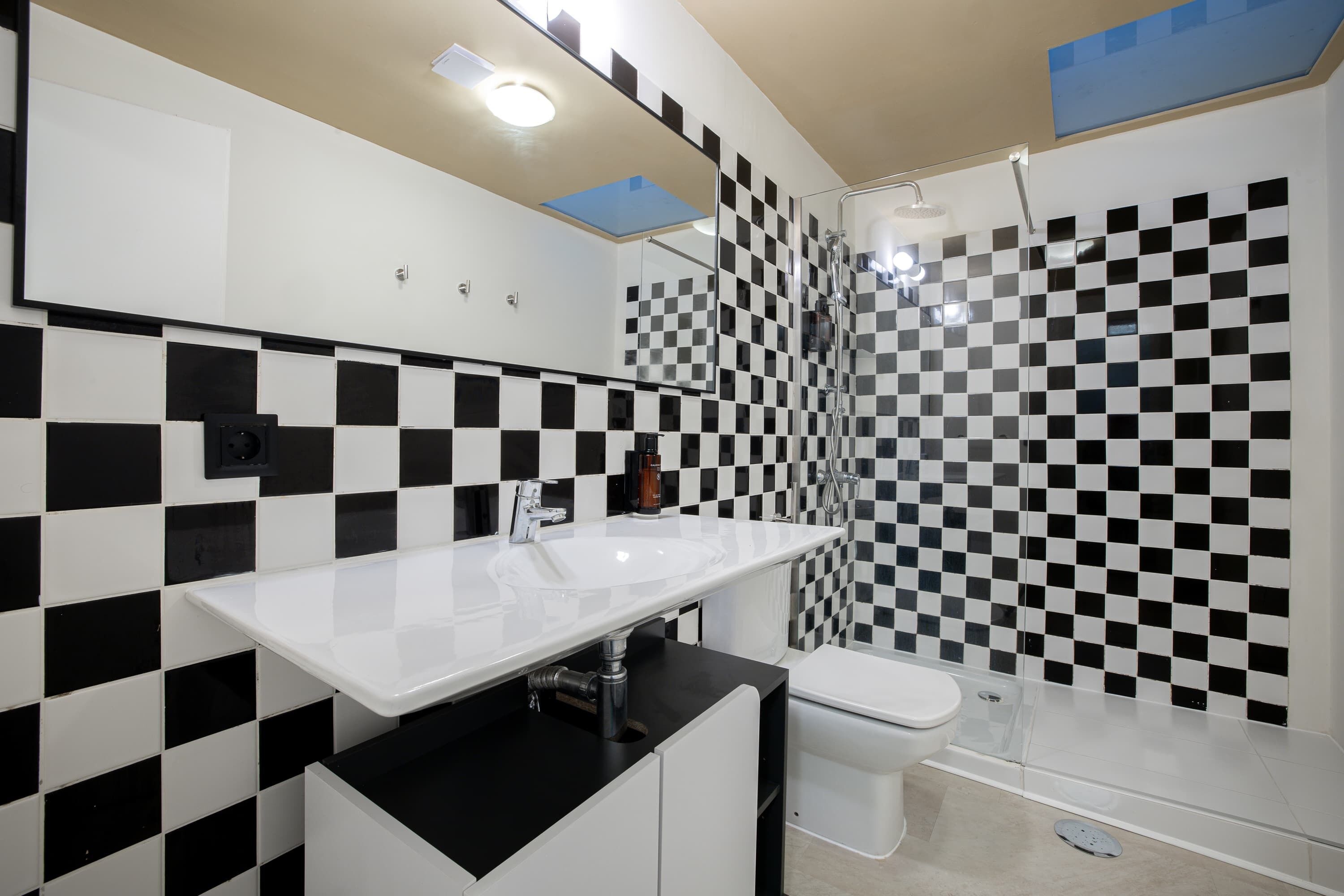 A modern bathroom with a checkered black and white tile wall, a white sink, and a glass shower enclosure.