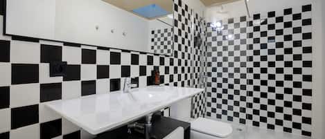 A modern bathroom with a checkered black and white tile wall, a white sink, and a glass shower enclosure.
