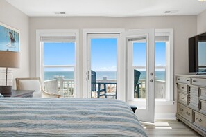 A bedroom with a large bed, a TV, a dresser, and a balcony with a view of the ocean. - Experience beachfront luxury at the Resolute, a spacious 4-bedroom escape in Oak Island. (Oak Island)