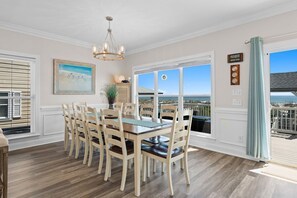 A dining area with a wooden table and chairs, a chandelier, a painting, and a view of the beach through large windows. - Experience beachfront luxury at the Resolute, a spacious 4-bedroom escape in Oak Island. (Oak Island)