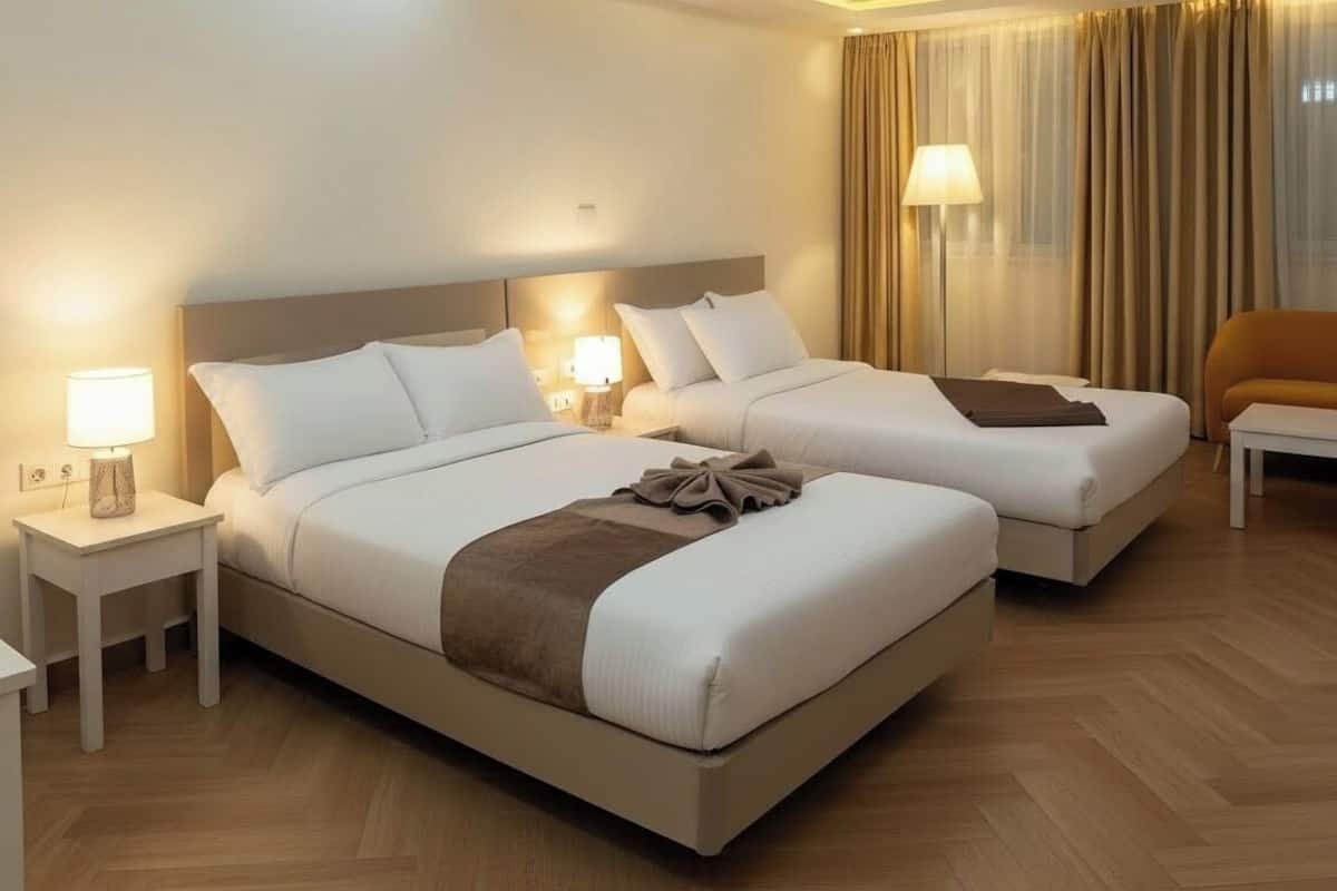 A hotel room with two beds, a sofa, a nightstand with a lamp, and a window with curtains.