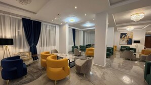 A modern hotel lobby with a marble floor, multiple seating areas with yellow and green chairs, a large chandelier, and a large painting on the wall. - Golden Gate Hotel (Awassa)