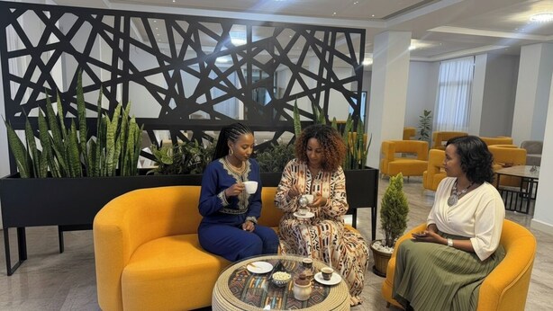 Three people seated on yellow sofas in a modern lounge area with a geometric wall design and potted plants. - Golden Gate Hotel (Awassa)