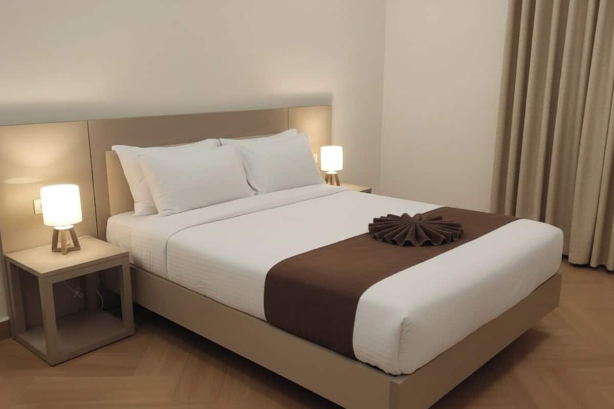 A modern hotel room with a large bed, two bedside tables with lamps, a decorative brown accent on the bed, and a view of the curtains.