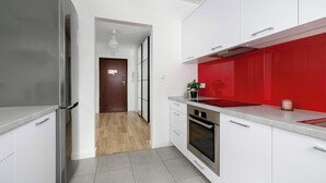 Una cocina moderna con armarios blancos, un salpicadero rojo y un refrigerador de acero inoxidable.