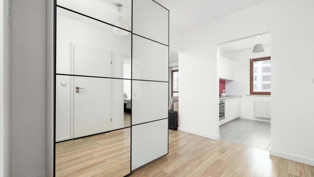 Un apartamento moderno con piso de madera, un armario blanco y una cocina visible a través de un umbral abierto.