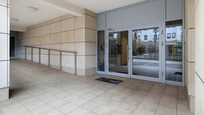 Una entrada moderna de edificio con suelo de baldosas, puertas de cristal y barandilla metálica.