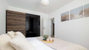 Un dormitorio con cama, almohadas, una bandeja con tazas y una planta, junto con tres cuadros decorativos con motivos playeros.